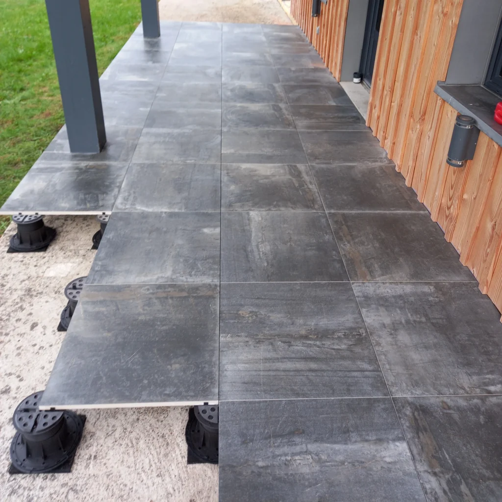 Photo d'une terrasse sur plots avec du carrelage gris foncé.