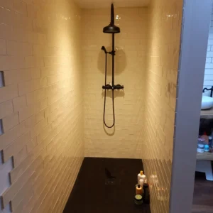 Photo d'une douche, avec du carrelage blanc et un bac à douche noir.